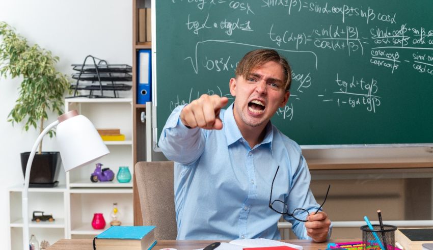 A man pointing at a blackboard in a classroom.