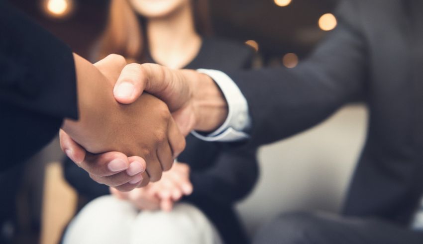 Two business people shaking hands in front of a group of people.