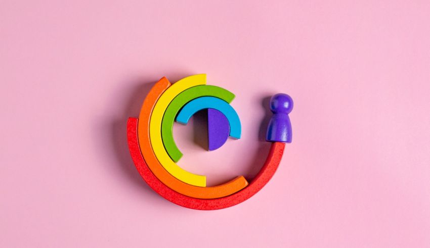 A rainbow colored wooden figure on a pink background.