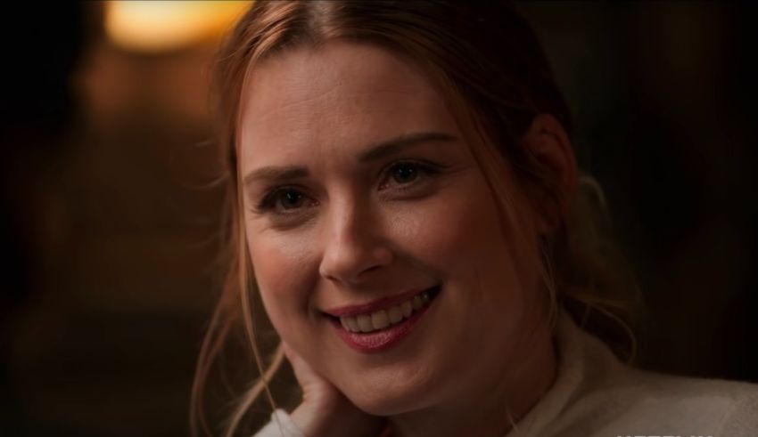 A woman with red hair smiling in a dark room.