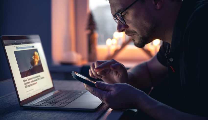 A man is using a laptop and a cell phone.