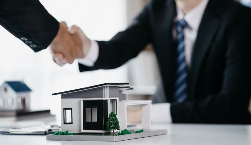 Two businessmen shaking hands over a model house.