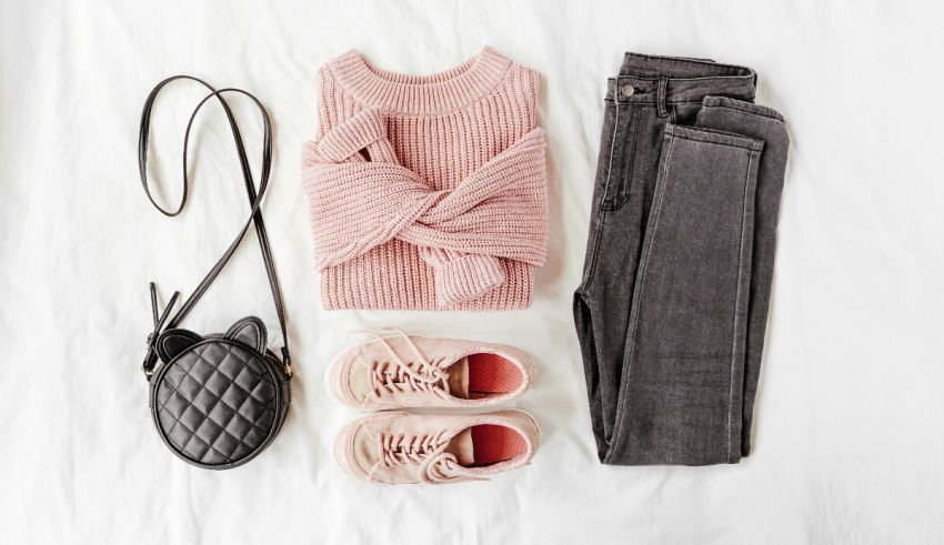 A pink sweater, jeans and purse are laid out on a bed.