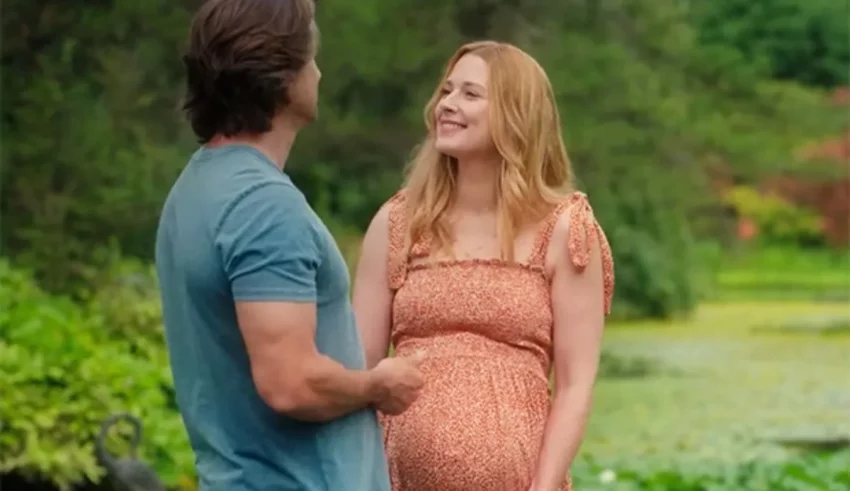 A pregnant woman and man standing next to a pond.