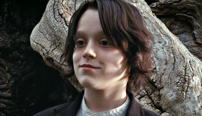 A young boy in a suit standing next to a tree.