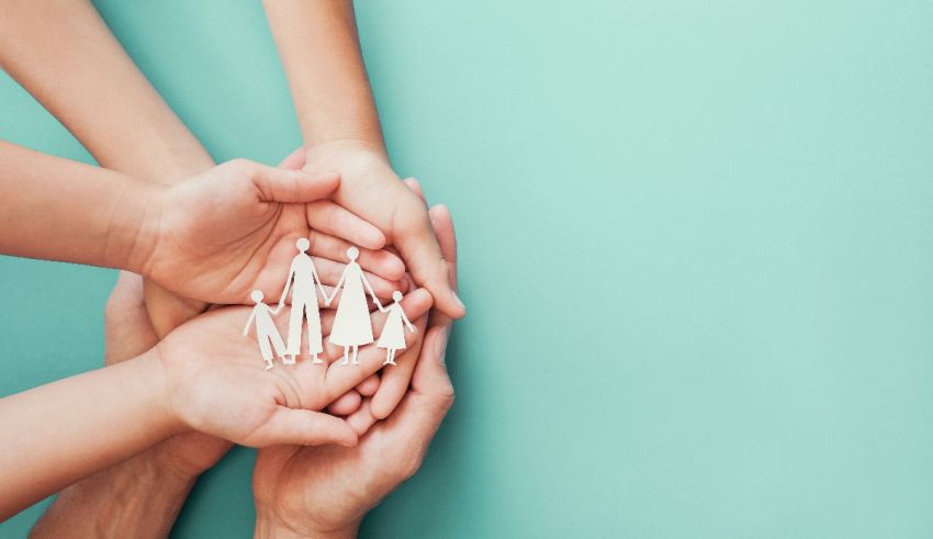 A group of hands holding a paper family on a turquoise background.