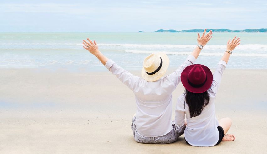 Two people sitting on the beach with their arms raised.