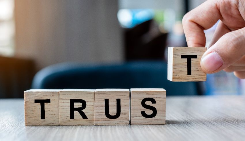 A hand holding a wooden block with the word trust on it.