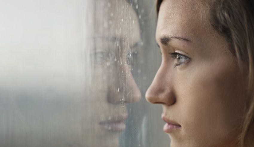 A woman looking out of a window with rain on her face.