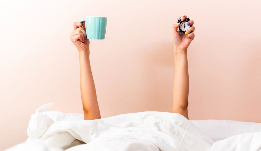 A woman laying in bed with a cup of coffee and a cookie.