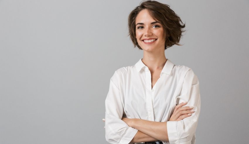 A smiling business woman with her arms crossed over gray background.