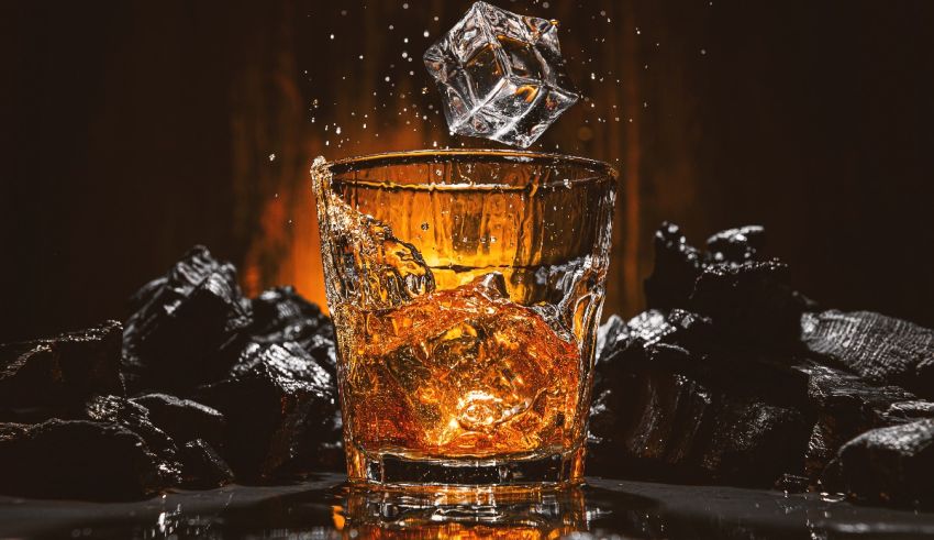 A glass of whiskey is being poured into a glass on a dark background.