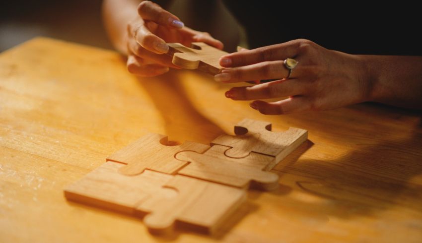 A person holding a wooden jigsaw puzzle on a table.