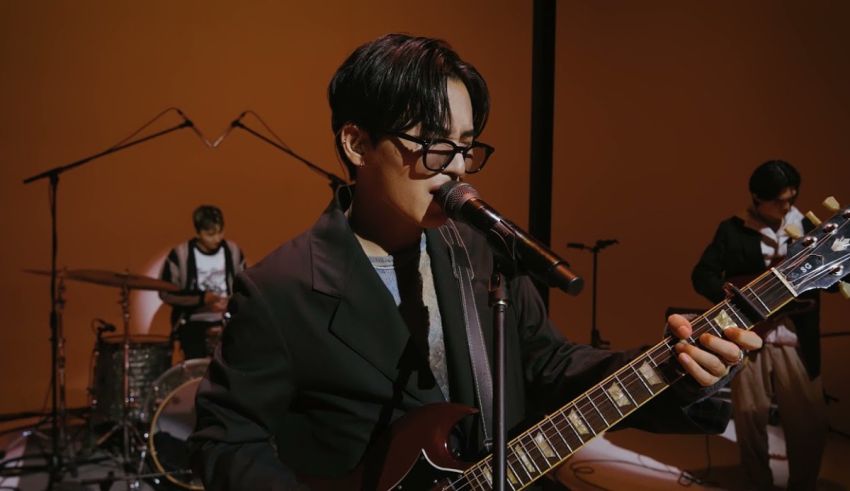 A man in glasses is playing a guitar in front of a microphone.