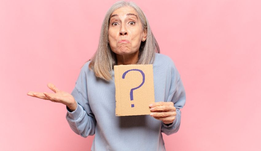 Senior woman holding a question mark on a pink background.