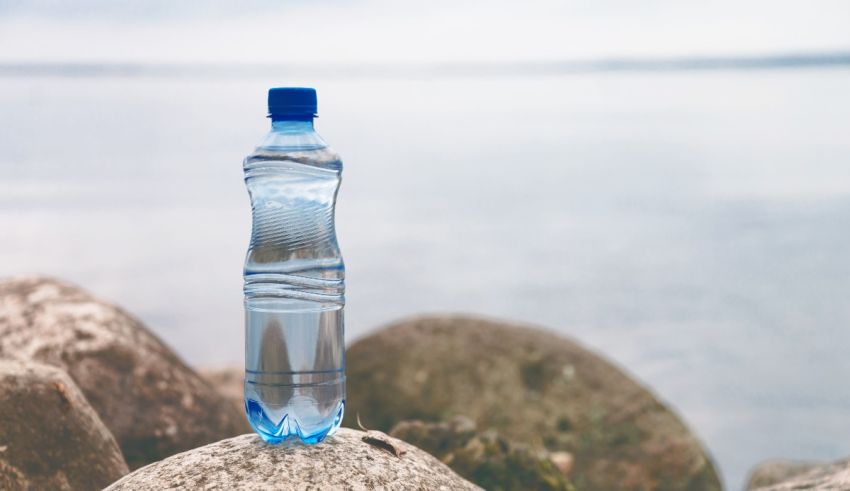 A bottle of water sits on a rock next to a body of water.