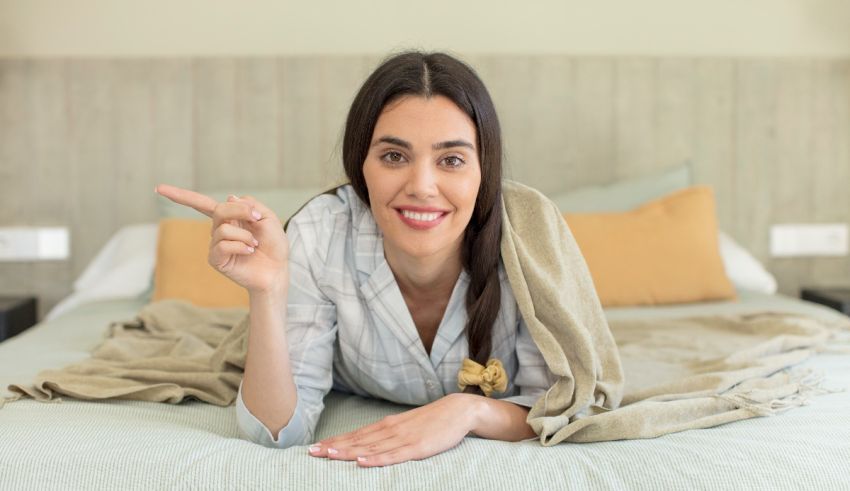 A young woman laying on a bed and pointing at something.