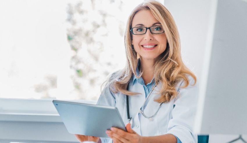 A female doctor holding a tablet in front of a computer.