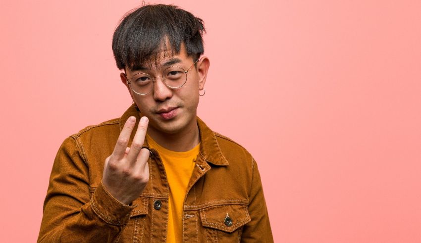 A young asian man making a v sign on a pink background.