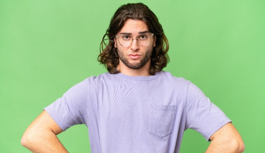 A young man with glasses posing against a green background.