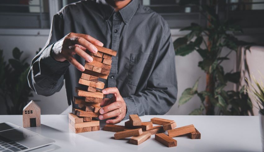 A man is stacking wooden blocks in front of a laptop.