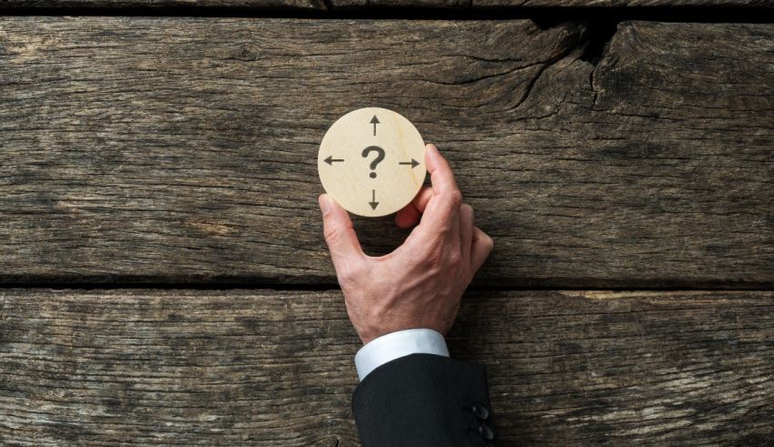 A businessman holding a question mark on a wooden background.