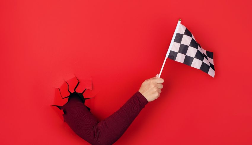 A woman holding a checkered flag through a hole in a red wall.