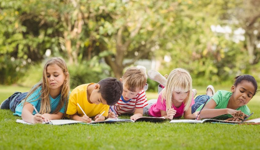 A group of children laying on the grass and writing.