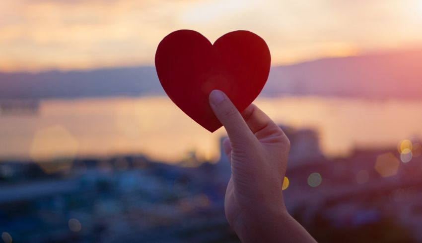 A woman is holding up a red heart in front of a city.