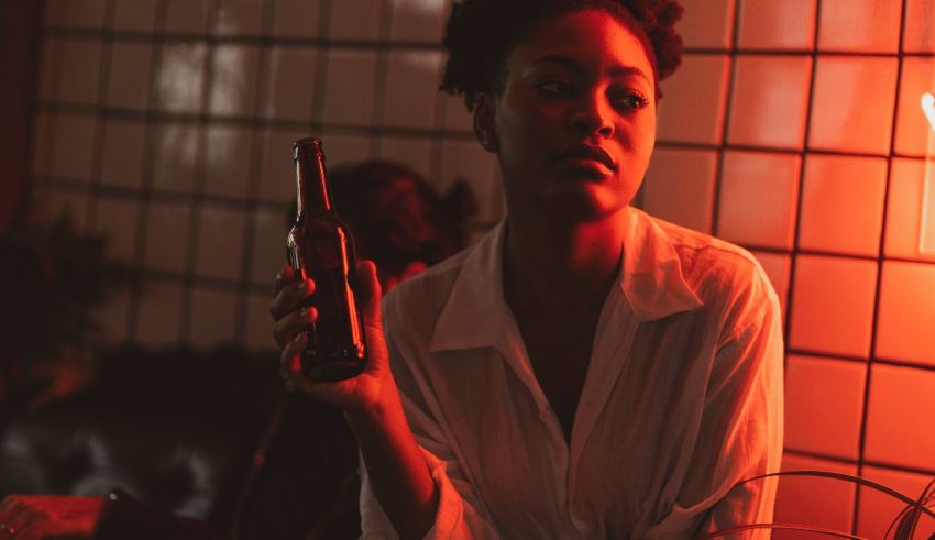 A woman holding a beer bottle in front of a red light.