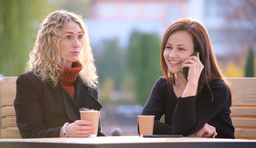 Two women talking on the phone while sitting at an outdoor table.