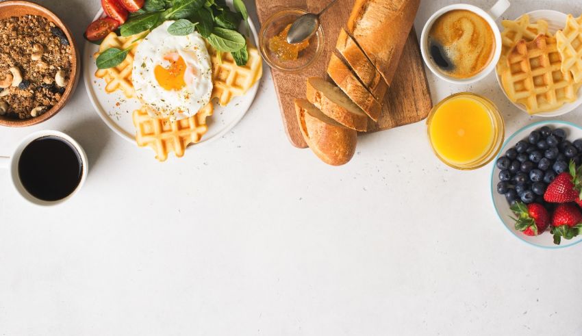 Breakfast with waffles, eggs, fruit and coffee on a white table.