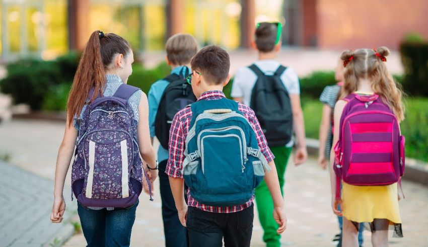 A group of children with backpacks walking down a sidewalk.