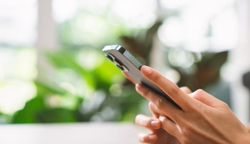 A woman's hand holding a cell phone in front of a window.