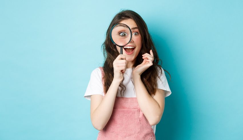 A young woman looking through a magnifying glass on a blue background.