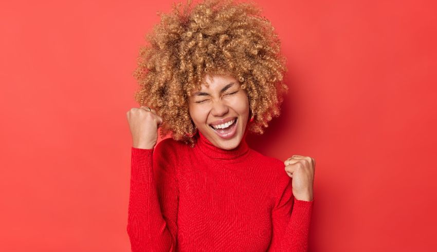 A young woman with afro hair is celebrating on a red background.
