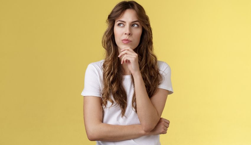 A young woman with her hand on her chin looking at a yellow background.