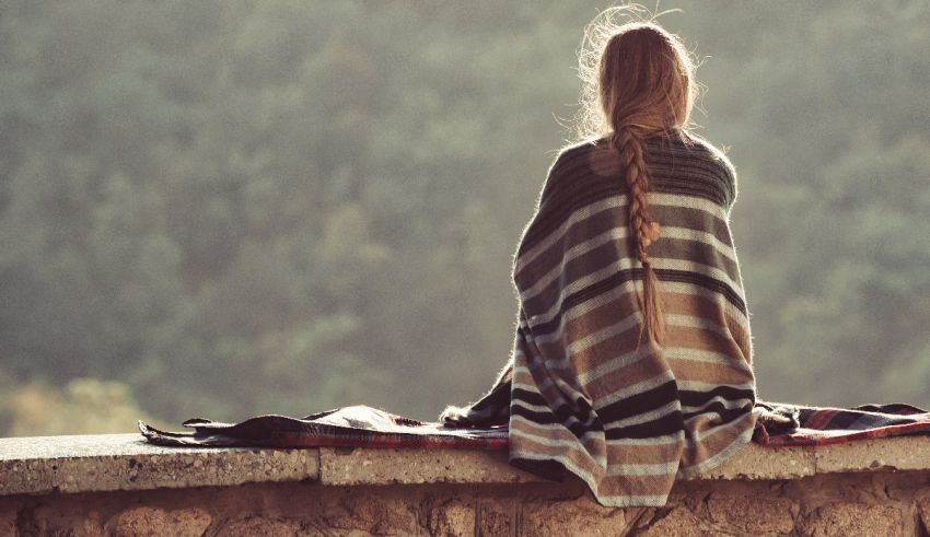 A woman sitting on a ledge with a blanket wrapped around her.