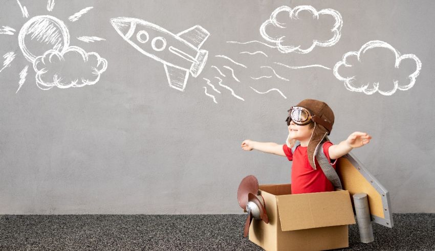 A young boy in a cardboard box with a rocket flying in the sky.