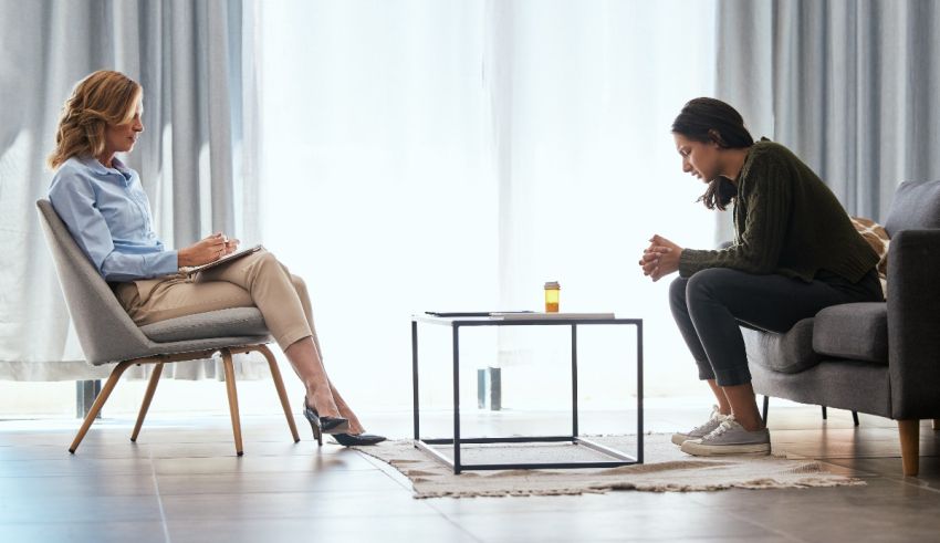 Two women sitting on a couch talking to each other.