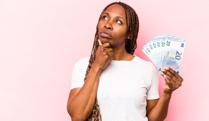 A young african american woman holding a stack of euro banknotes against a pink background.