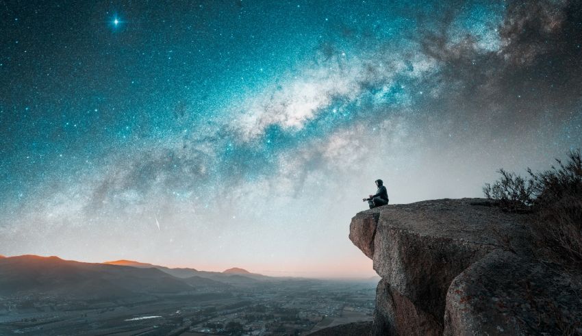 A man sitting on top of a mountain looking at the milky way.