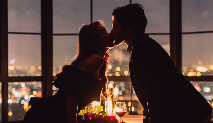 A couple kissing in front of a window at night.