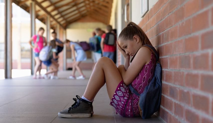 A girl sits on the floor of a school hallway.
