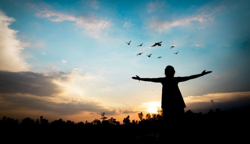 A silhouette of a man with his arms outstretched in front of a sunset.