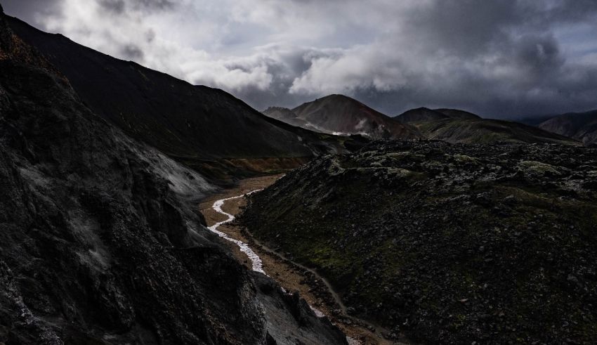 A river runs through the mountains under a cloudy sky.
