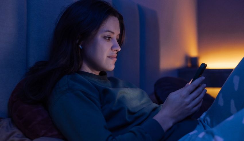 A woman is using her phone in bed at night.