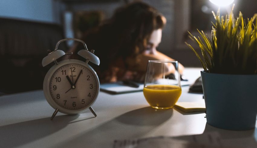 An alarm clock on a desk next to a glass of orange juice.